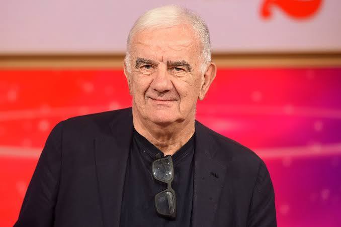 Gene Gnocchi sorridente in uno studio televisivo con giacca scura